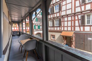 Ein Balkon mit zwei Stühlen, Blick auf traditionelle Fachwerkhäuser und ein kleines Fenster mit einer Tür.