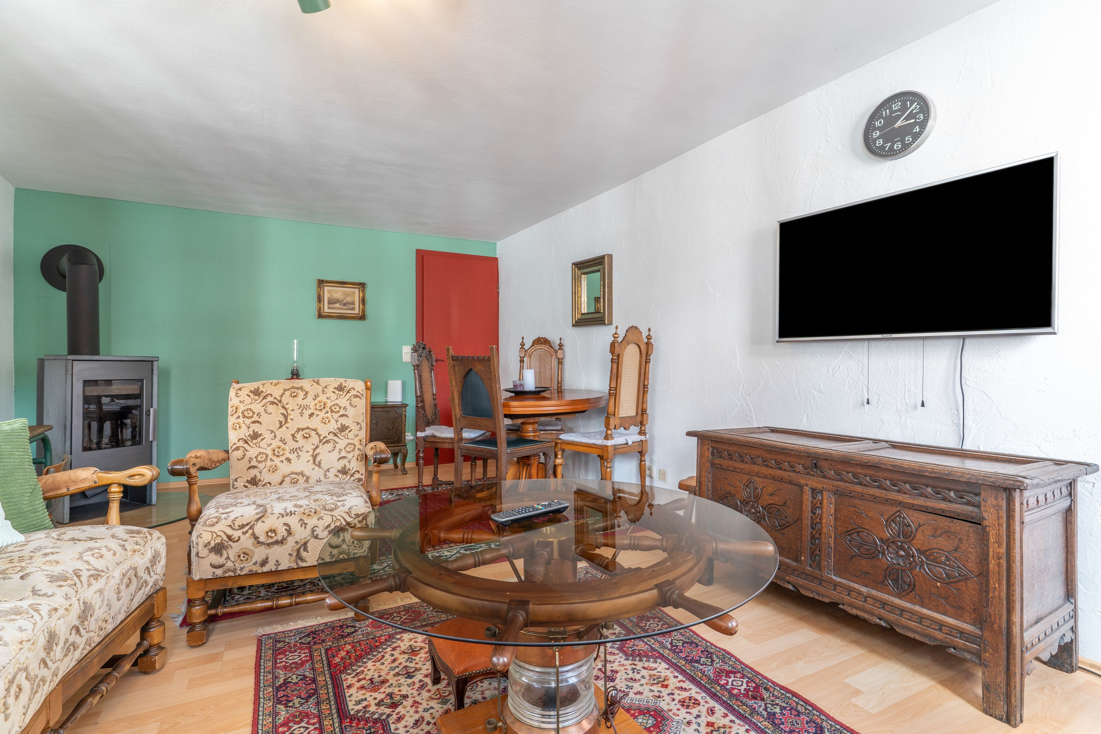 A living room with a glass table, wooden chairs, a television, and a fireplace.