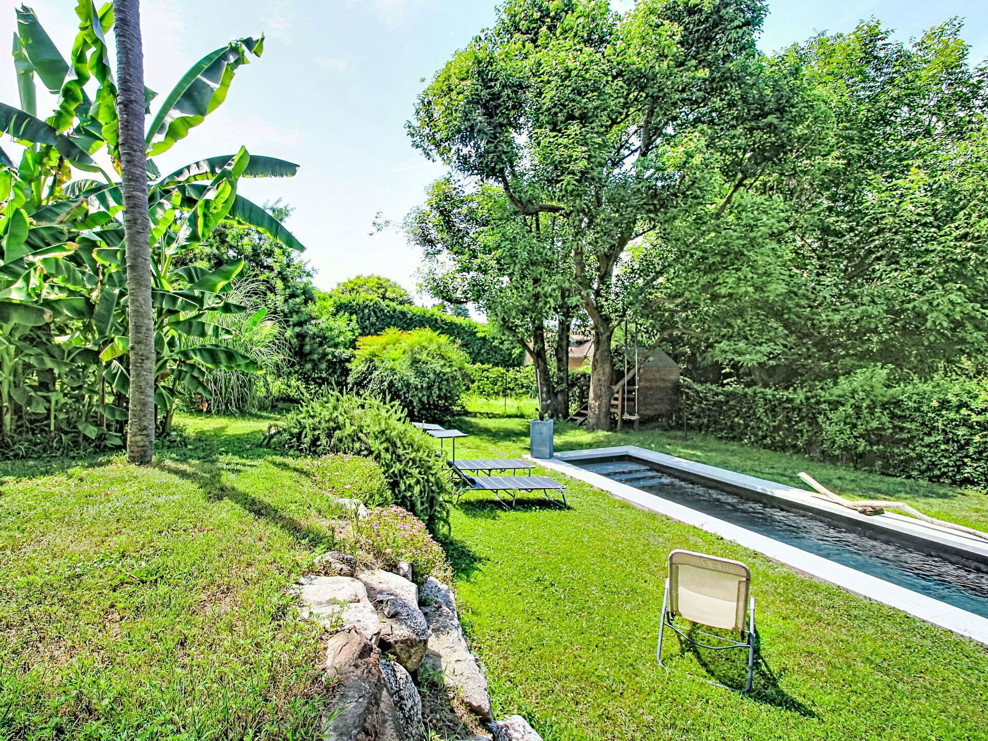 Un jardín cuidado con piscina, una pequeña cascada y un espacio para sentarse.