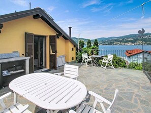 Eine Terrasse mit Tisch und Stühlen, Blick auf einen See und ein Gebäude mit einem Satteldach.