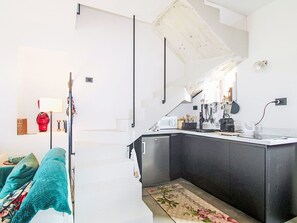 Eine moderne Küche mit einer Kochinsel, ein Essbereich inklusive Sofa und eine Treppe, die in ein Obergeschoss führt.