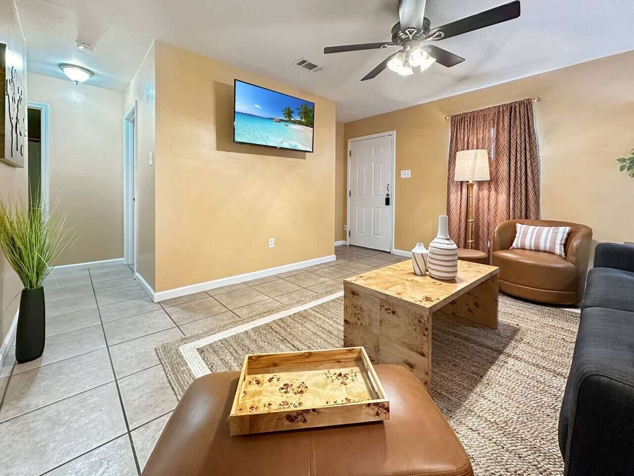 Un salon comprenant un téléviseur, un ventilateur de plafond, une table basse, un canapé et une porte.