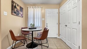 Un comedor con una mesa redonda y cuatro sillas, una puerta blanca y un cuadro colgado en la pared.
