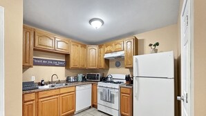 Una cocina con gabinetes de madera, un refrigerador blanco, una estufa, un microondas y un lavamanos.