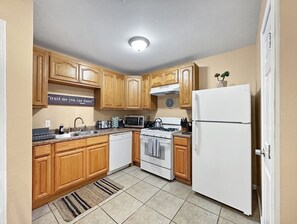 Eine Küche mit Holzausstattung, einem weißen Kühlschrank, einem Herd, einer Mikrowelle und einem Spülbecken.