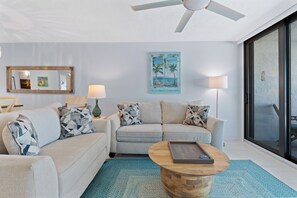 A modern living room with a ceiling fan, a sofa set, a coffee table, and a painting on the wall. - 🏖️Beachfront, Pool and Stunning Sunsets | Sunset Condo 502🌅 (Fort Myers Beach)
