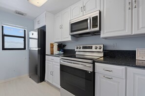 A modern kitchen with white cabinetry, a stainless steel refrigerator, a microwave, an oven, and a gas stove. - 🏖️Beachfront, Pool and Stunning Sunsets | Sunset Condo 502🌅 (Fort Myers Beach)