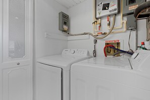 A laundry room with a white washing machine, a control panel, and a water heater. - 🏖️Beachfront, Pool and Stunning Sunsets | Sunset Condo 502🌅 (Fort Myers Beach)