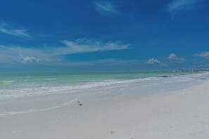 A beach with a clear sky, calm sea, and distant buildings. - 🏖️Beachfront, Pool and Stunning Sunsets | Sunset Condo 502🌅 (Fort Myers Beach)