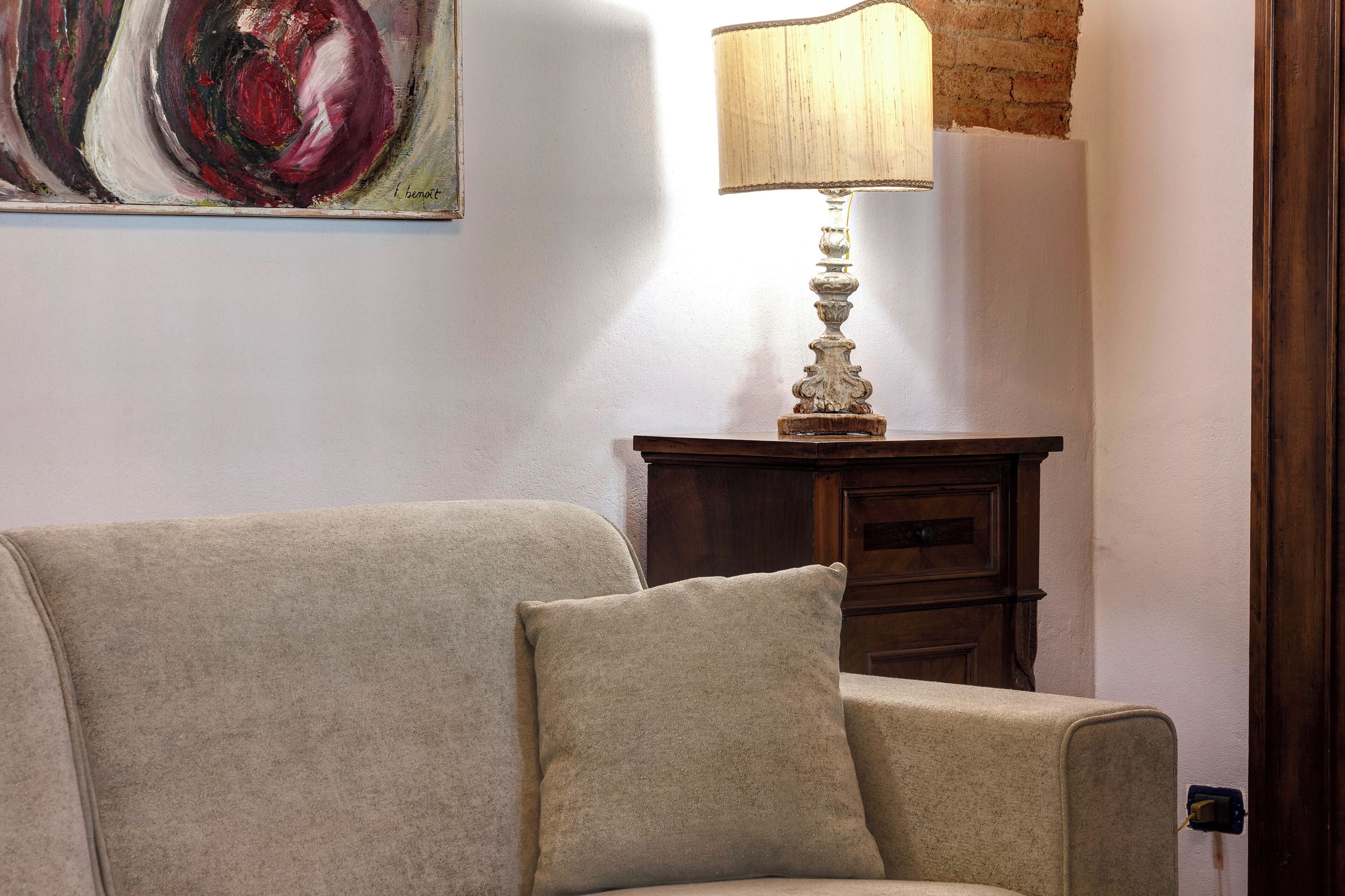Un soggiorno con un divano color beige, una lampada su un tavolino in legno e un quadro appeso al muro.