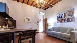 Un'area pranzo con tavolo e sedie in legno, una cucina con fornello e un soggiorno con divano e un quadro.