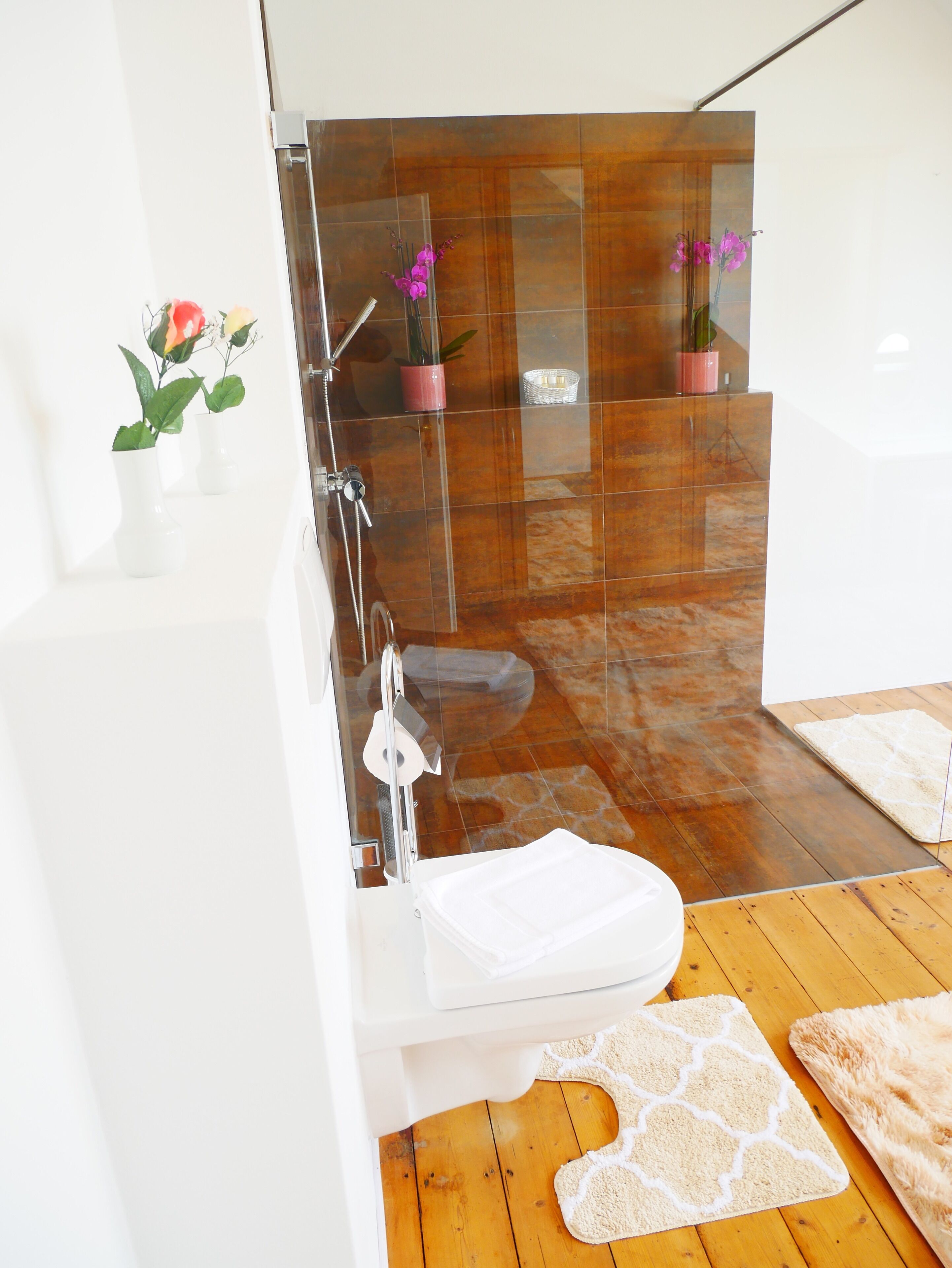 A modern bathroom with a glass-enclosed shower, a white sink, and a wooden floor.