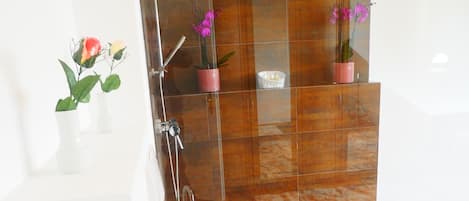Een moderne badkamer met een douchecabine van glas, een wit wastafeltje en een houten vloer.