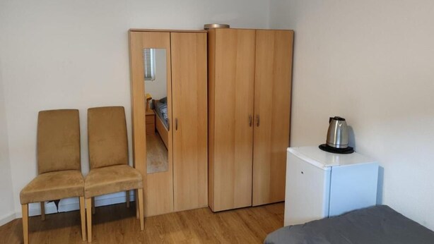 A room with a wardrobe, a small kitchenette, and two chairs. - Monteurzimmer Mühlheim am Main (Mühlheim)