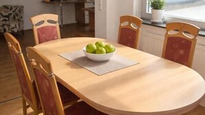 A dining table with six chairs, a bowl of apples, and a window with a view of trees. - Monteurzimmer Mühlheim am Main (Mühlheim)