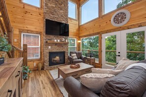 Ein gemütliches Wohnzimmer mit Kamin aus Stein, Holzmöbeln und großen Fenstern.