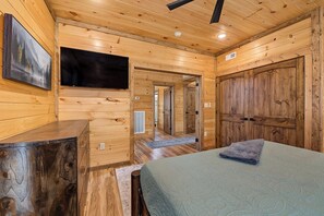 A wooden cabin interior with a bed, a flat-screen TV, and a large wooden door. - Cloud 9 Lodge: Private Heated Indoor Pool, Theater & Game Room, Sleeps 12 (Sevierville)