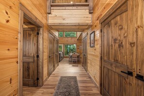 A wooden interior hallway with a central rug, wooden doors, and a view of an outdoor area with greenery. - Cloud 9 Lodge: Private Heated Indoor Pool, Theater & Game Room, Sleeps 12 (Sevierville)