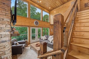 A wooden interior with a staircase, a sofa, a coffee table, and a TV mounted on a stone wall. - Cloud 9 Lodge: Private Heated Indoor Pool, Theater & Game Room, Sleeps 12 (Sevierville)