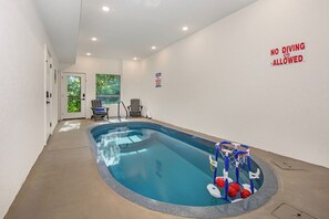 Piscina interior com um cesto de basquete, um aviso de 'NÃO MERGULHAR' e uma porta que dá para o exterior.