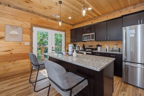 A modern kitchen with wooden walls, a central island, bar stools, and stainless steel appliances. - Cloud 9 Lodge: Private Heated Indoor Pool, Theater & Game Room, Sleeps 12 (Sevierville)