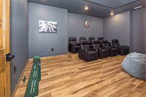 Ein Zimmer mit Holzboden, einer grünen Matte, schwarzen Stühlen, einem Sitzsack und zwei gerahmten Bildern an der Wand.