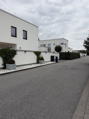 Eine moderne Wohnstraße mit weißen Gebäuden, einem gepflasterten Weg und einer Hecke.