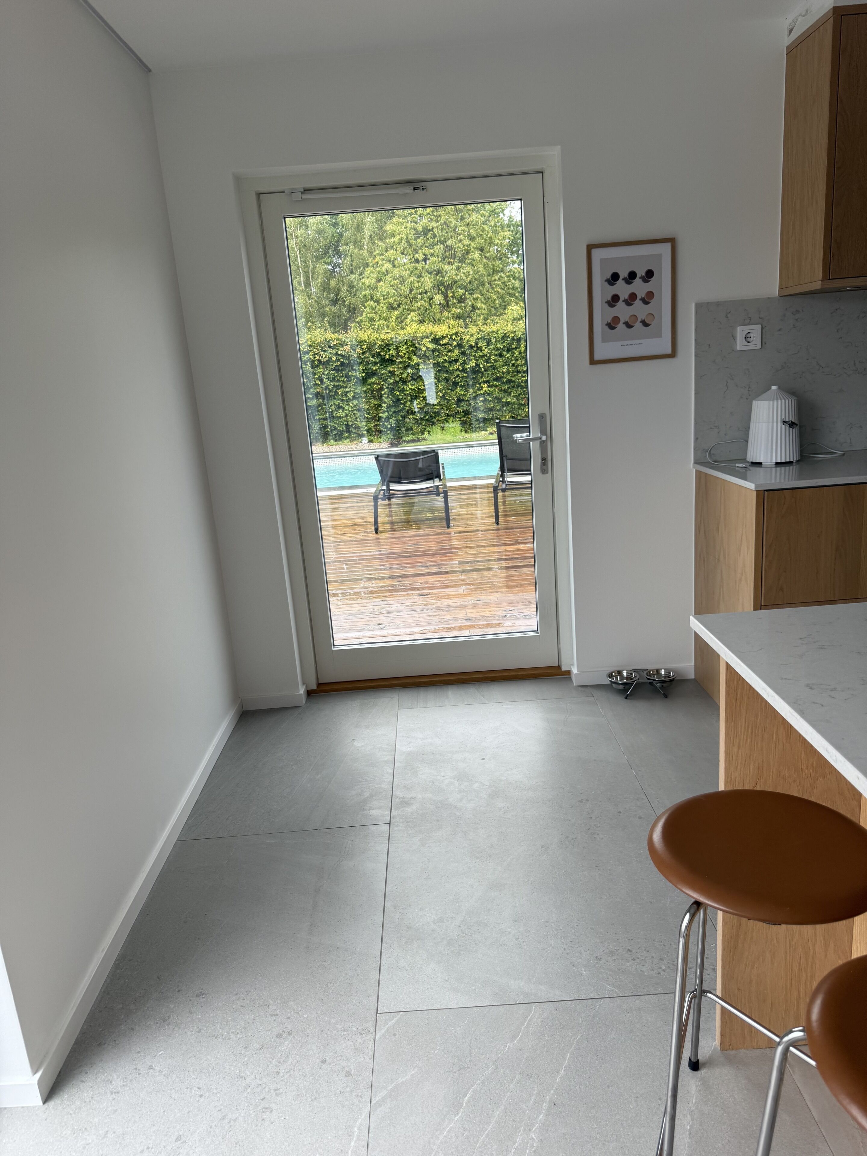 A kitchen with a view of a pool, a framed picture on the wall, and a dog bowl on the floor.