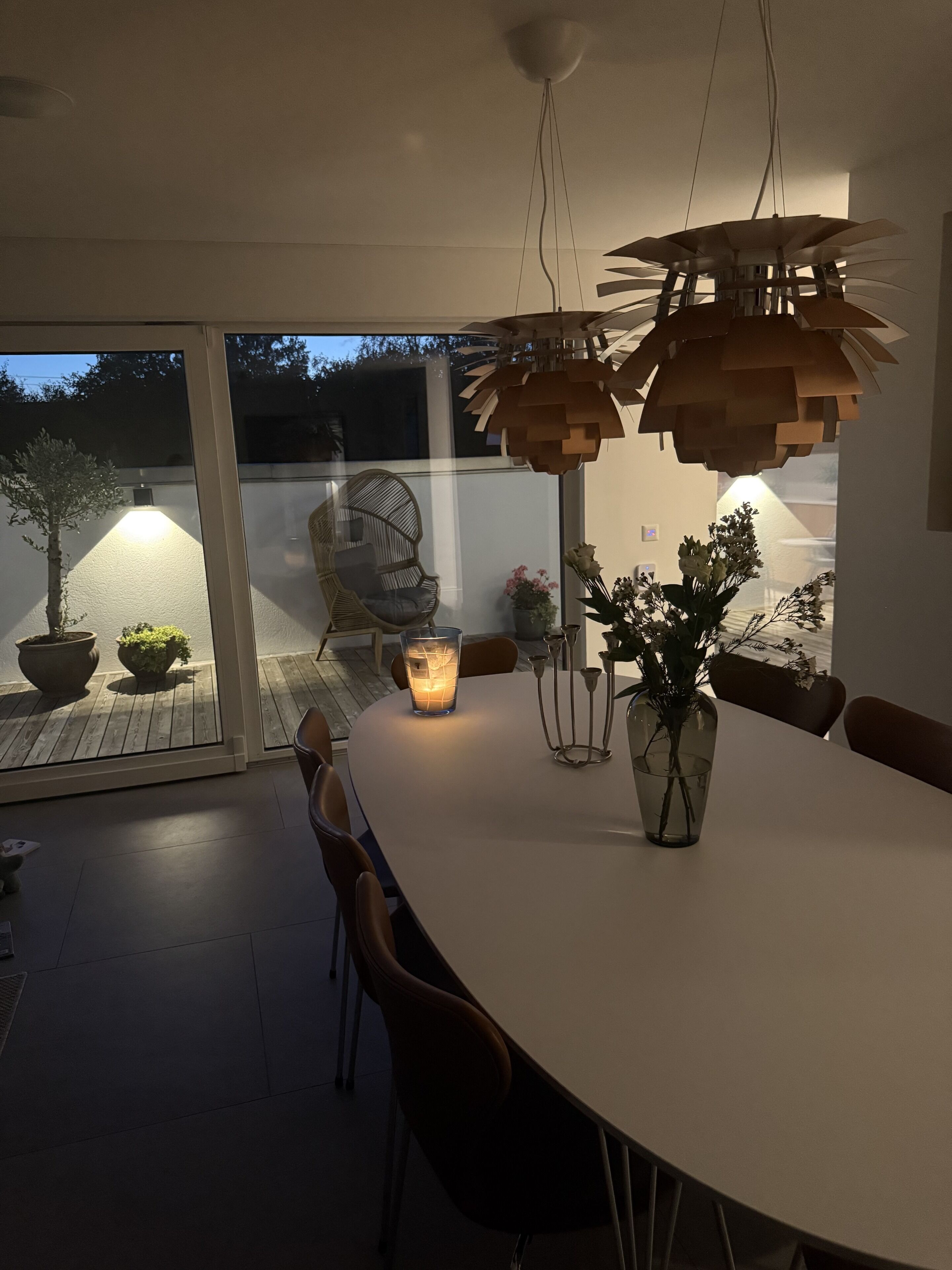 Un coin repas avec une table ronde, des chaises, un luminaire suspendu et des plantes en pot.