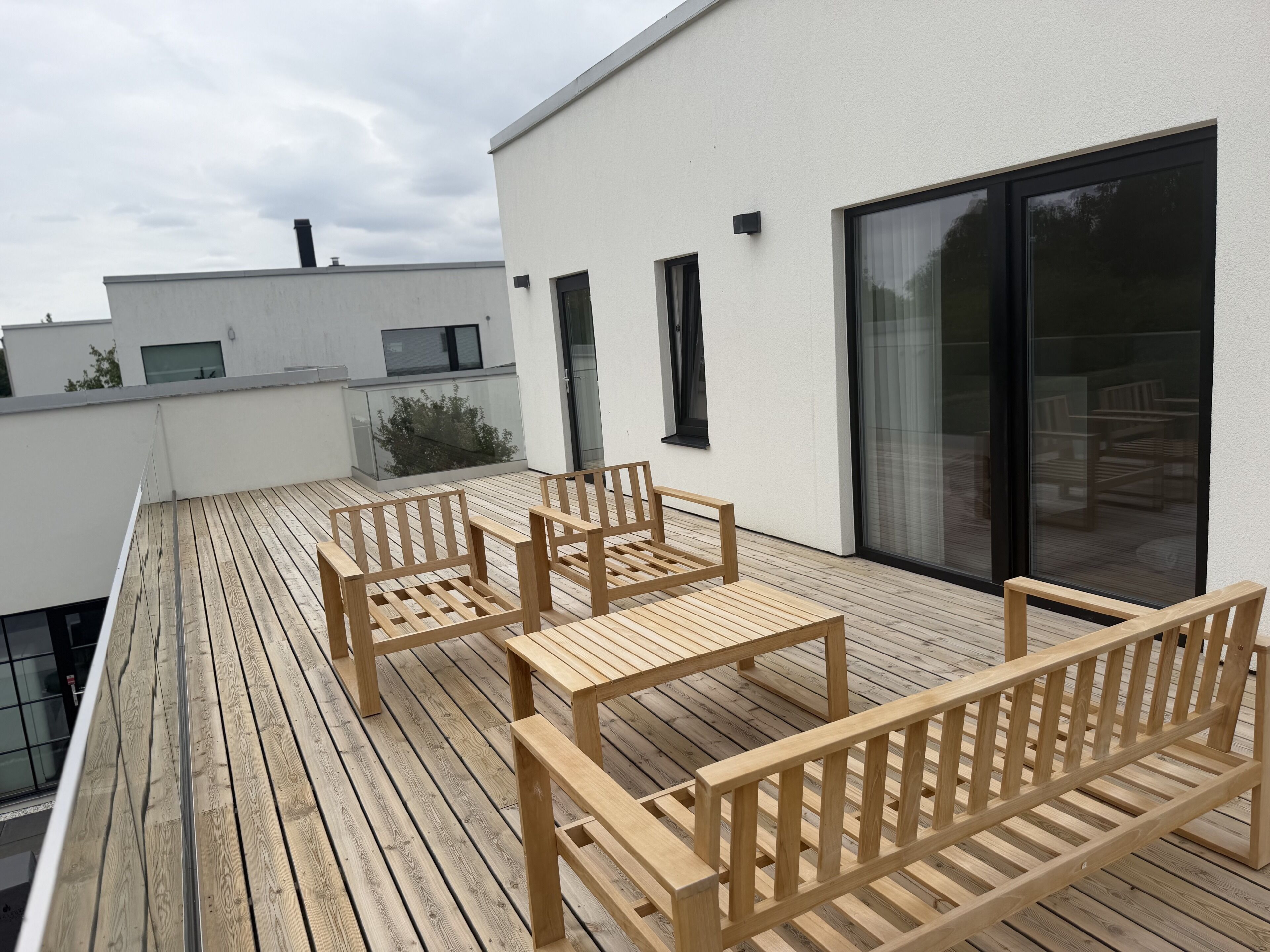 A wooden deck with outdoor furniture, a glass door, and a white building facade.