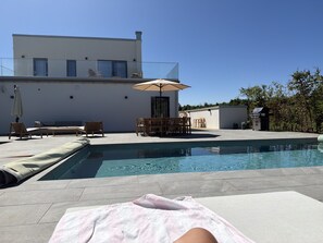 A swimming pool with lounge chairs and a table, surrounded by a modern building with a flat roof.