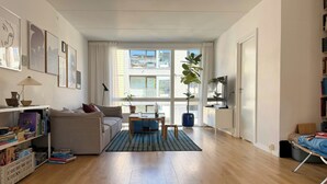 Un salon avec un canapé, une table basse et un téléviseur. On y trouve également des étagères et une plante en pot.