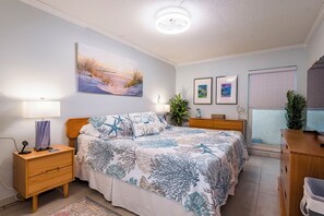 Ein Schlafzimmer mit einem Bett, Nachttischen, einem Schreibtisch, einer Lampe, einer Pflanze und Kunstwerken an den Wänden.