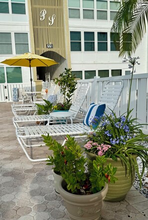 Un espace de détente aménagé sur le toit, avec des chaises longues blanches, un parasol jaune et des plantes en pot.