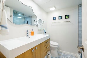 Et moderne badeværelse med et hvidt håndvaskarrangement, toilet, bruseområde og et håndklædestativ.