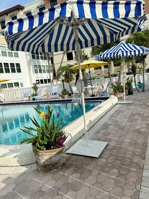 Un espace aménagé au bord de la piscine, avec des chaises longues, des parasols et des plantes en pot.