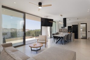 A modern living space with a large sliding glass door, a dining area, and a kitchen. - Luxurious Villa Poseidon - With Private Pool (Bali)