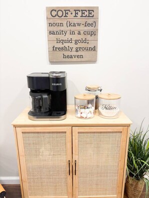 Une machine à café est posée sur un meuble en bois, à côté de laquelle se trouvent deux récipients étiquetés « crémier » et « filtres ».