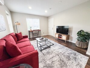 Ein Wohnzimmer mit einem roten Sofa, einem Glastisch und einem Fernseher auf einem Holzboden.
