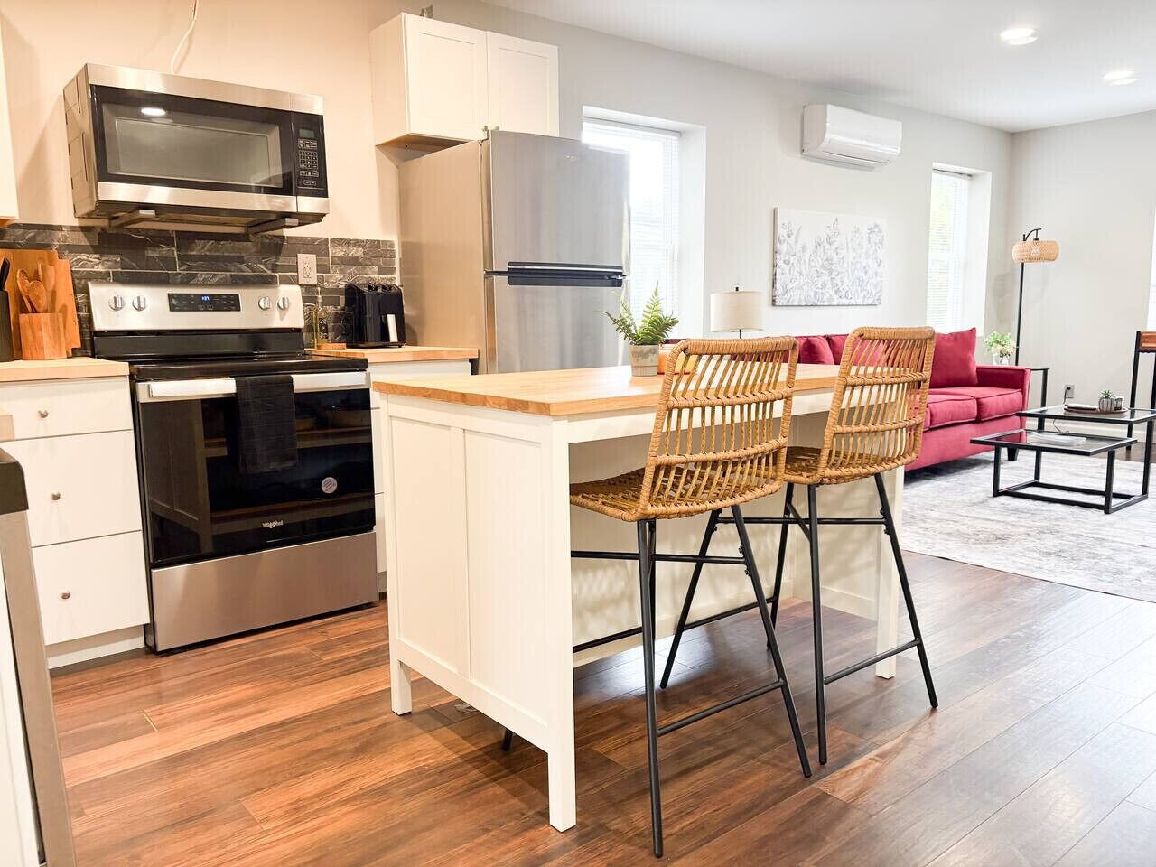 A modern kitchen with a built-in microwave, oven, and refrigerator. There are two wicker chairs at a wooden island counter.