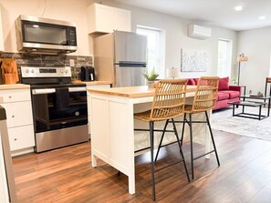 A modern kitchen with a built-in microwave, oven, and refrigerator. There are two wicker chairs at a wooden island counter.