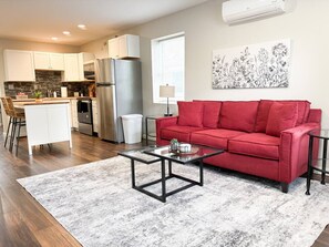 Ein modernes Wohnzimmer mit einem roten Sofa, einem Glastisch und einer Küche im Hintergrund.