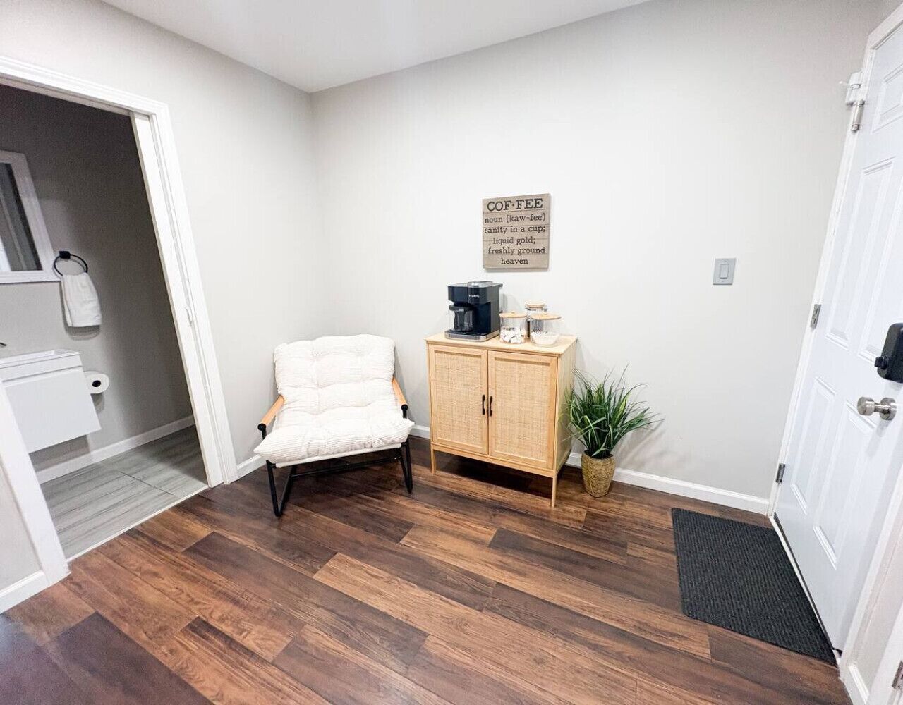 Une pièce avec une chaise blanche, un meuble en bois, une plante en pot et une porte.