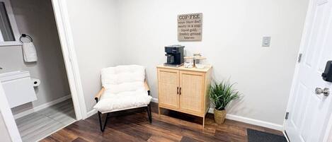Une pièce avec une chaise blanche, un meuble en bois, une plante en pot et une porte.