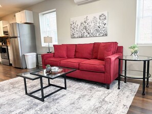 A modern living room with a red sofa, a glass coffee table, and a kitchen area in the background.