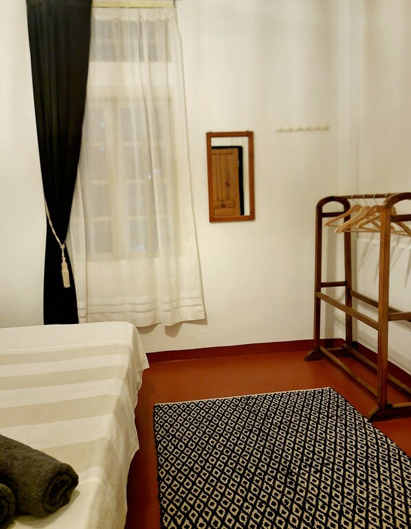 A bedroom with a bed, a wooden bunk bed, a window with sheer curtains, a patterned rug, and a wall-mounted mirror.