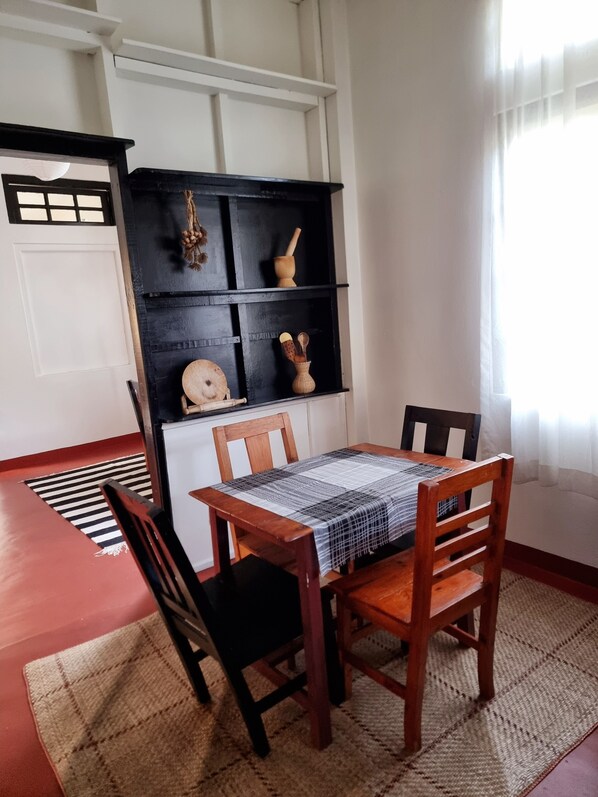 A dining area with a table set for two, a black shelf with kitchen utensils, and a view of the outside through a window.