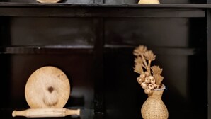 A black shelf with three wooden items: a round plate, a wooden bowl with a handle, and a woven vase with dried flowers.