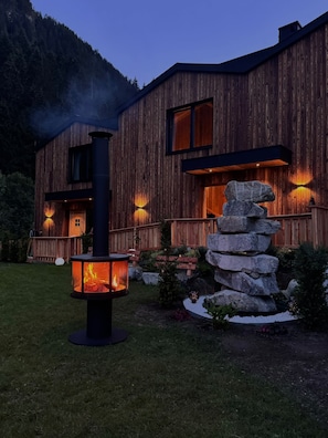 A wooden cabin with a fireplace and stone feature in the yard. - SLOW Fine Chalets (Neustift im Stubaital)
