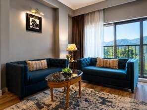 A modern living room with two sofas, a coffee table, and a large window with a mountain view.